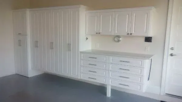 A garage with lots of white cabinets and drawers.