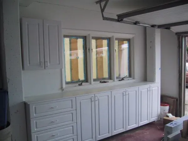 A room with white cabinets and drawers and a window.