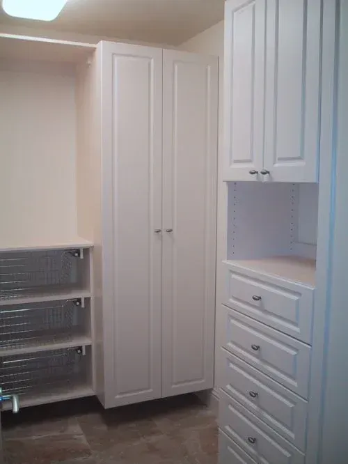 A walk in closet with white cabinets and drawers