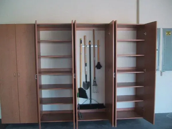 A broom and shovel are hanging on a rack in a cabinet