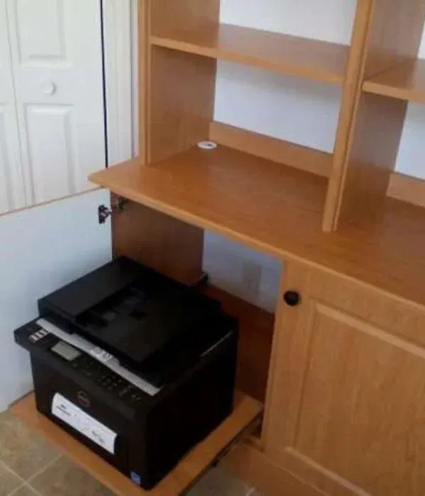 A printer is sitting under a wooden cabinet