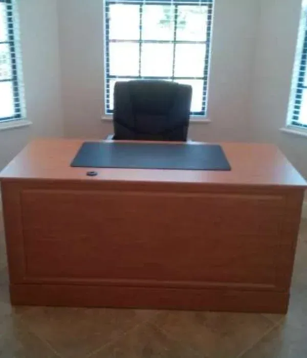 A wooden desk with a black chair in front of a window.