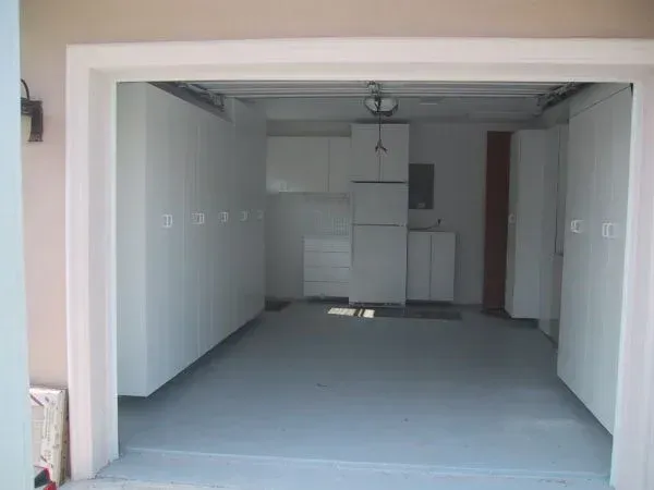 An empty garage with white cabinets and a refrigerator