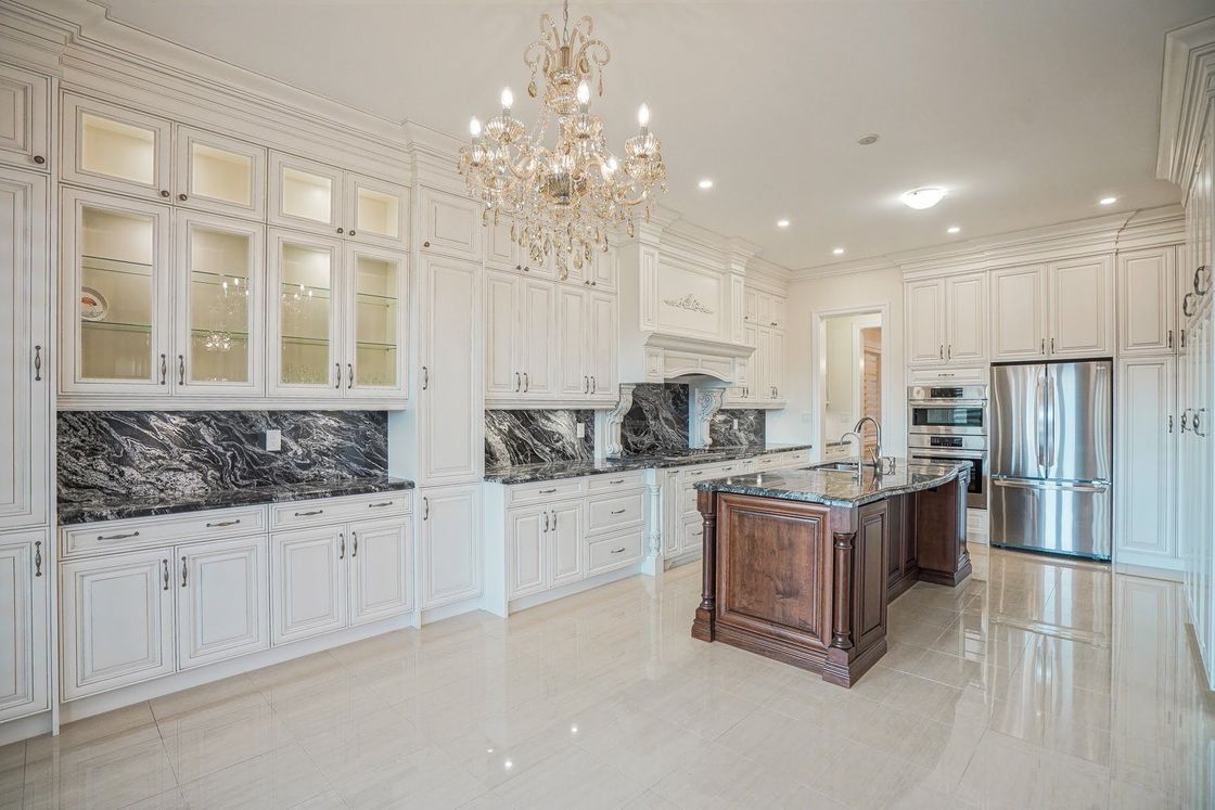 A large kitchen with white cabinets , granite counter tops , stainless steel appliances and a chandelier.