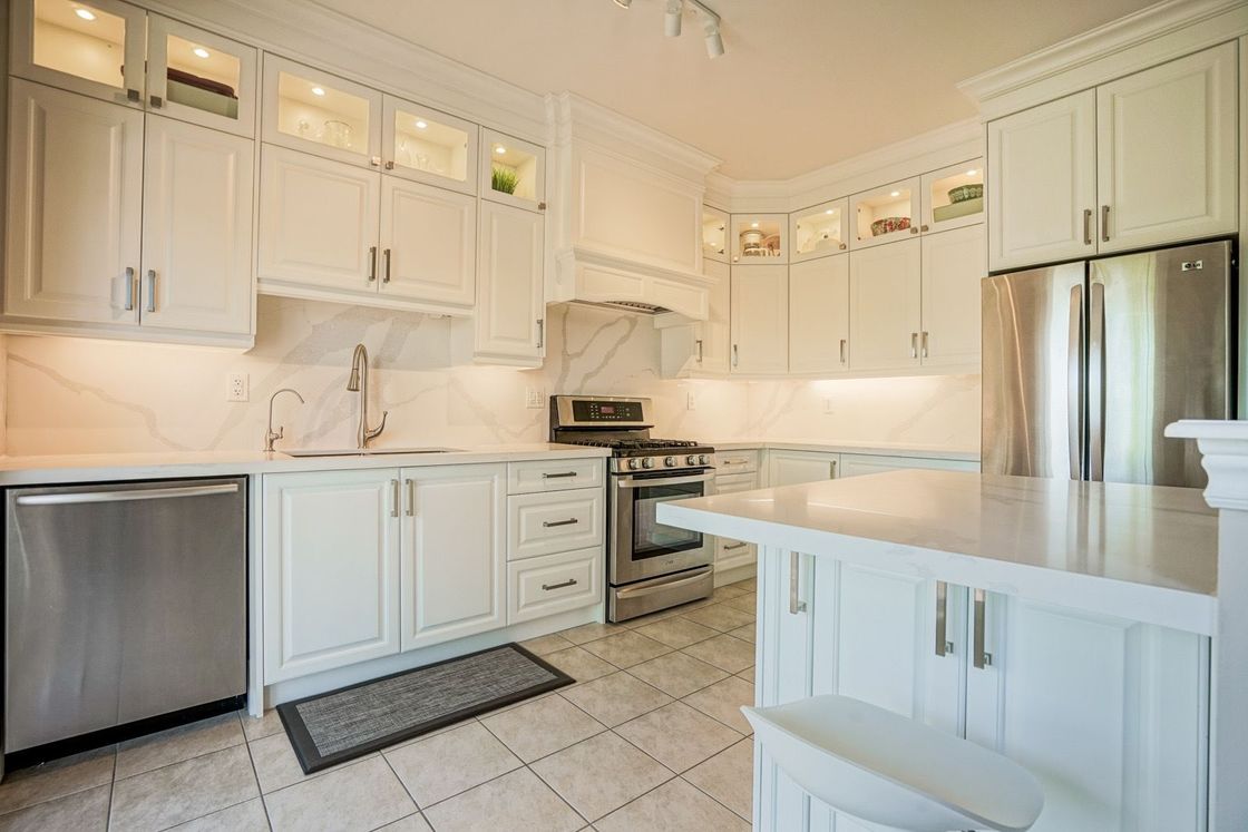 A kitchen with white cabinets , stainless steel appliances , and a large island.