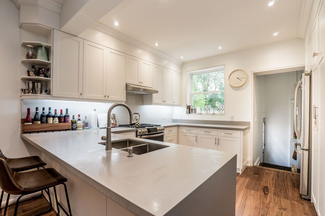 A kitchen with white cabinets , stainless steel appliances , a sink , and a clock on the wall.