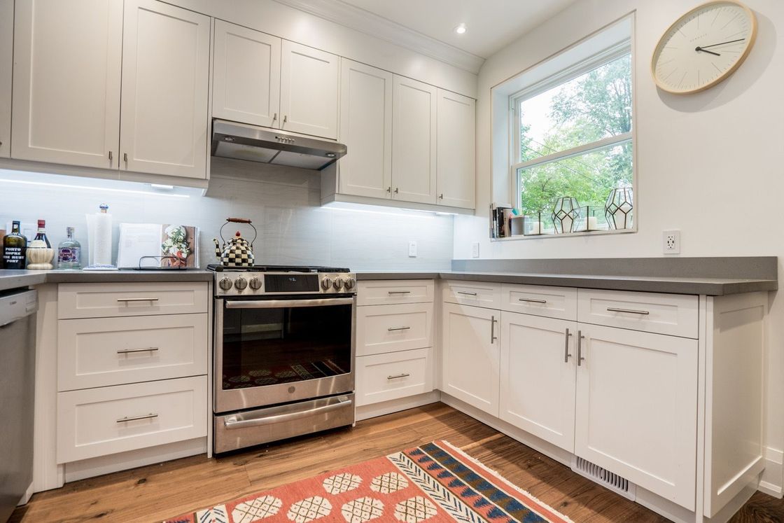 A kitchen with white cabinets , stainless steel appliances , a rug and a clock on the wall.