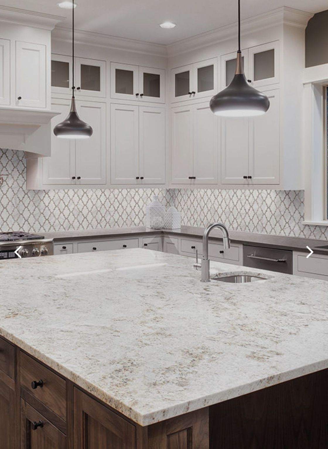 A kitchen with white cabinets and a large island with a sink.