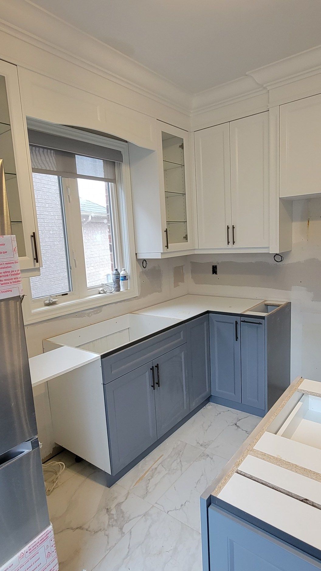 A kitchen with gray cabinets and white counter tops is being remodeled.