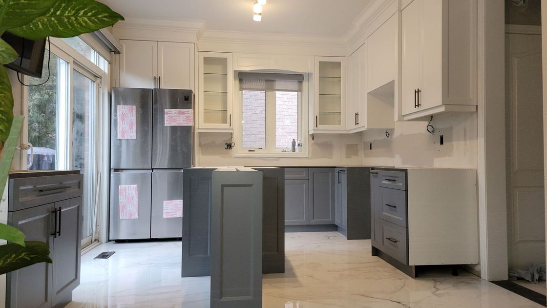 A kitchen with gray cabinets and white cabinets and a stainless steel refrigerator.