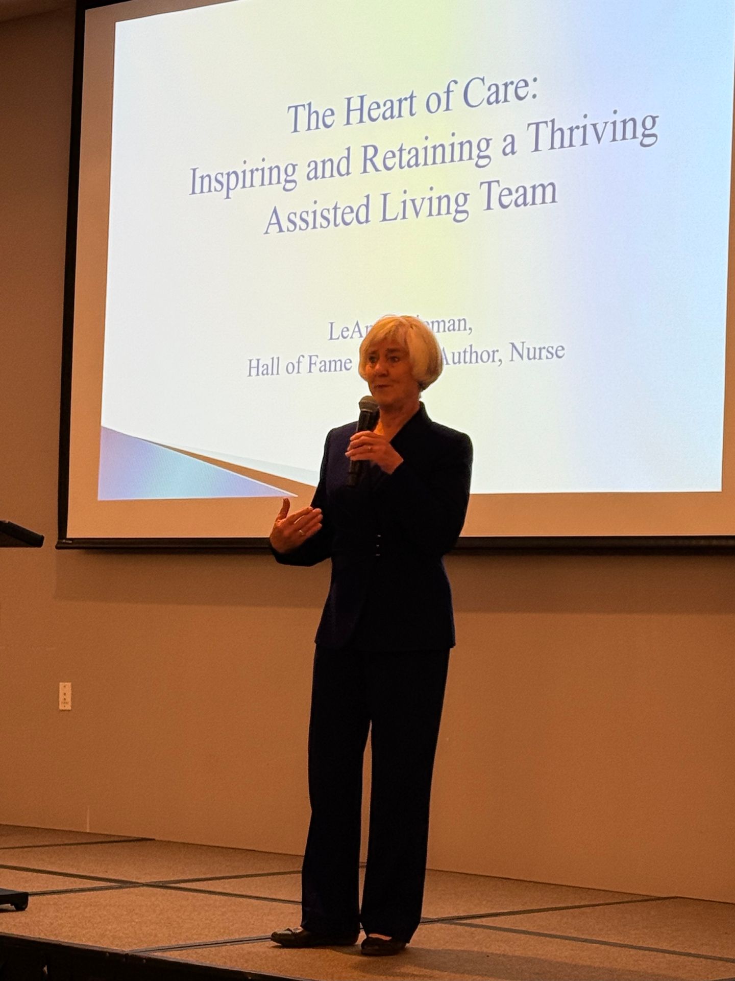 Woman presenting on stage; title slide reads 