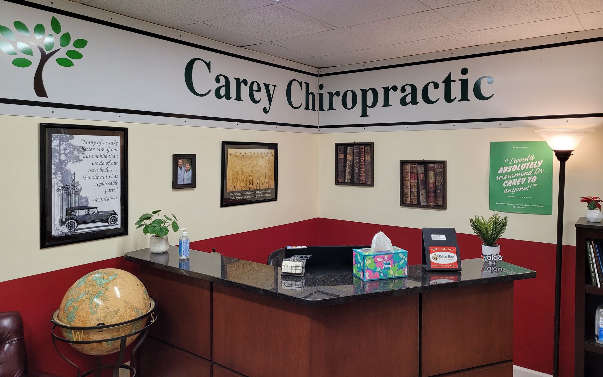 Reception area of Carey Chiropractic. Desk, framed art, globe, and sign on the wall.