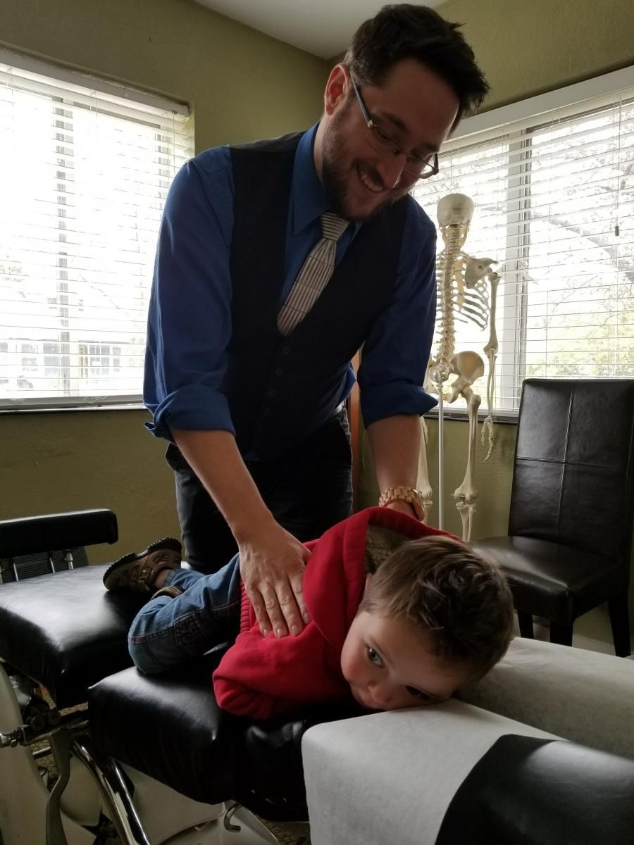 Chiropractor adjusts a young boy's back on a treatment table; smiles, indoor setting.