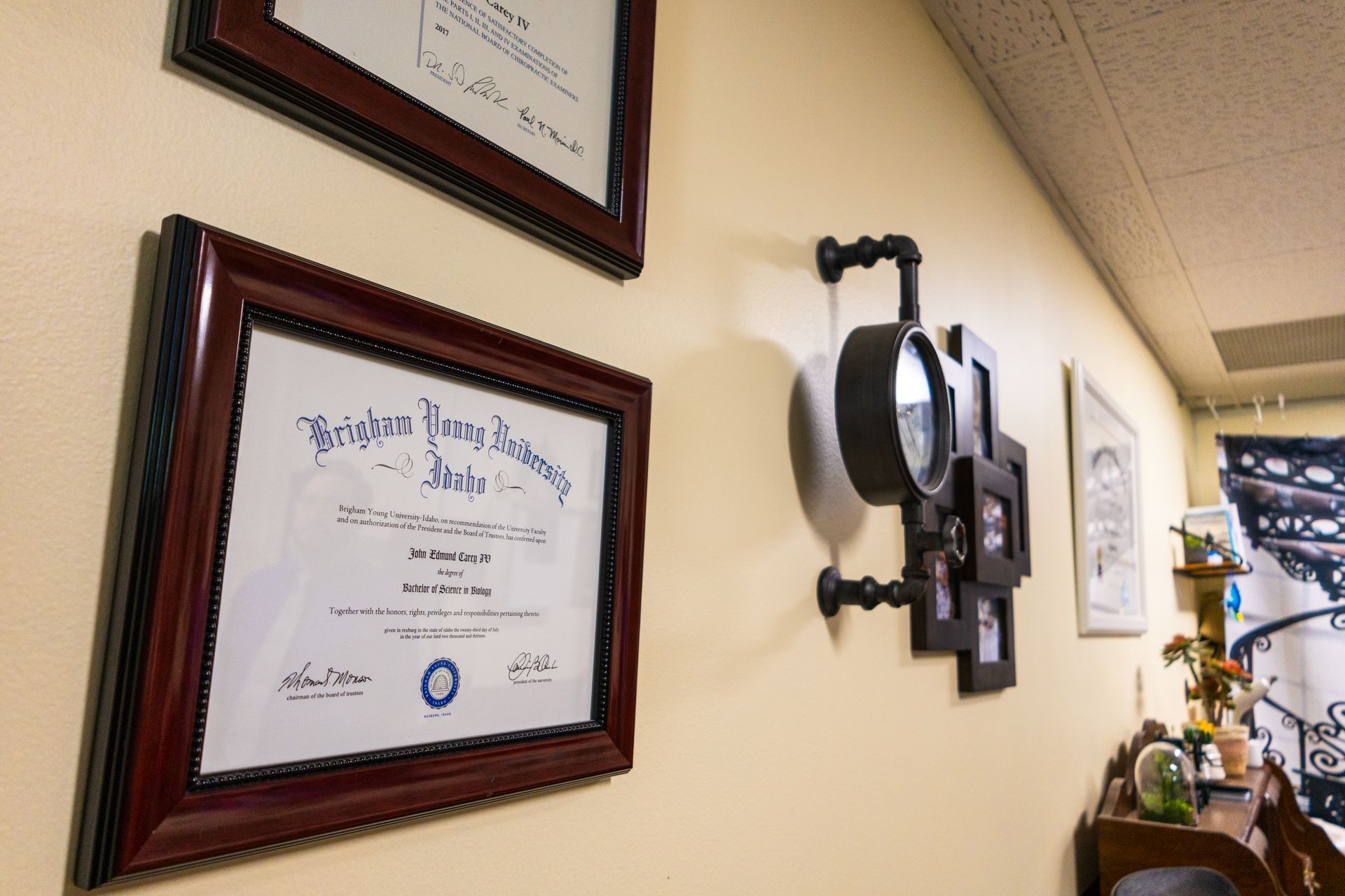 Wall with framed documents and decorative clock and picture frames.