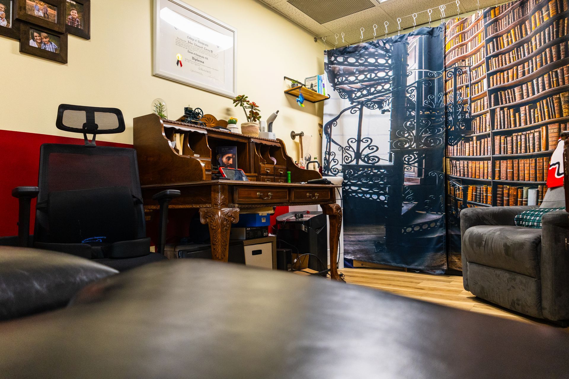 Antique desk in a home office with a black chair, bookcase curtain, and framed artwork.