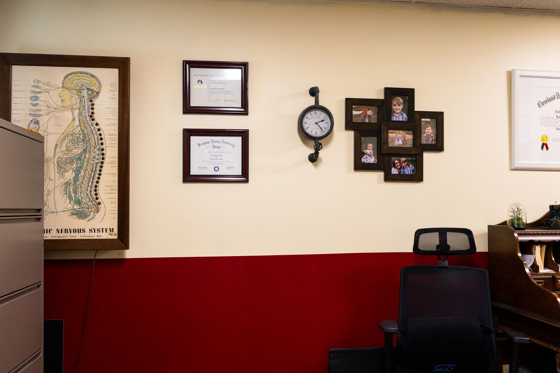 Office with red and beige walls. Artwork, clock, framed photos, and a chair are visible.