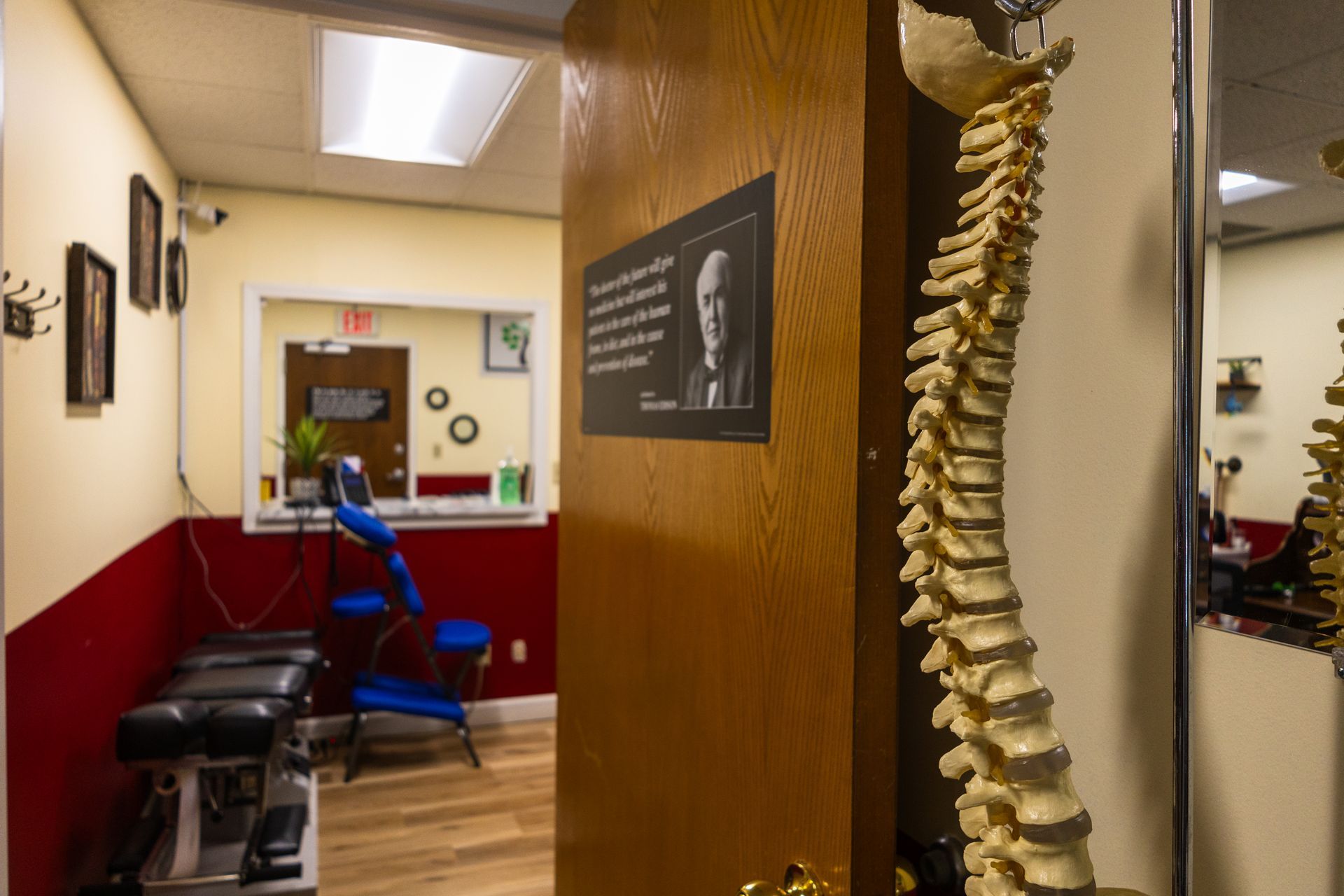 Chiropractic office with a spine model, treatment table, and doorway to a waiting area.