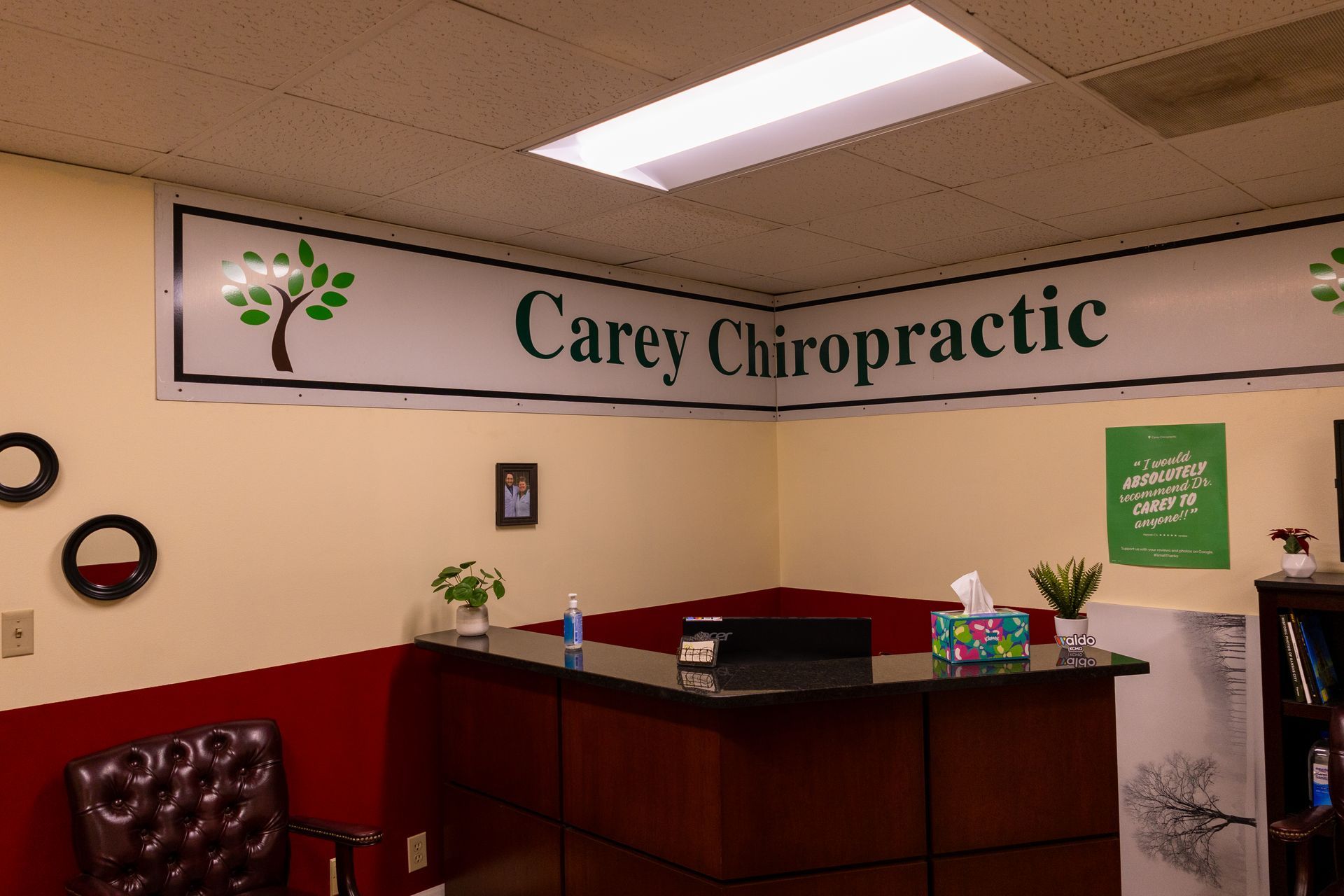 Carey Chiropractic office reception area: reception desk, sign, framed art, waiting area, beige and red walls.
