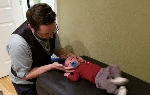 Man examining baby lying on a couch, baby wearing a pacifier and red onesie.