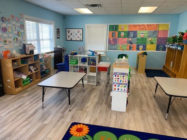 A classroom with tables , shelves , and a rug with a sunflower on it