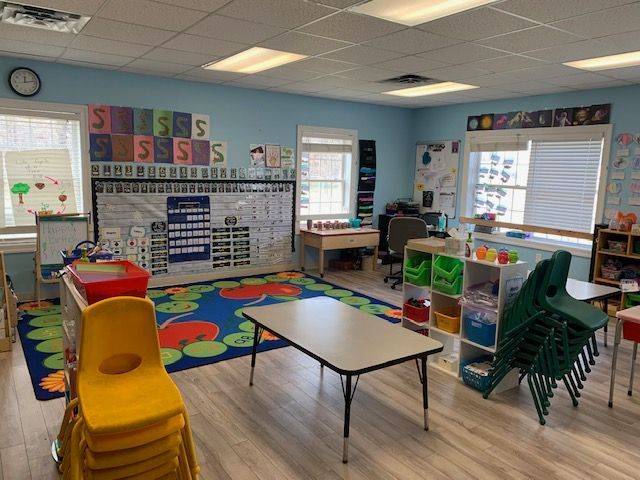 A classroom with a table , chairs , shelves and a rug.