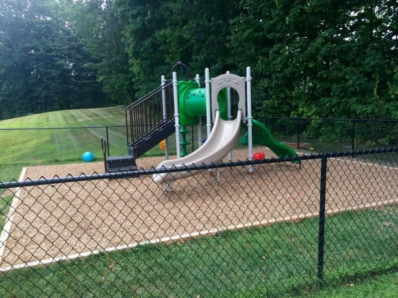 A chain link fence surrounds a playground with a green slide