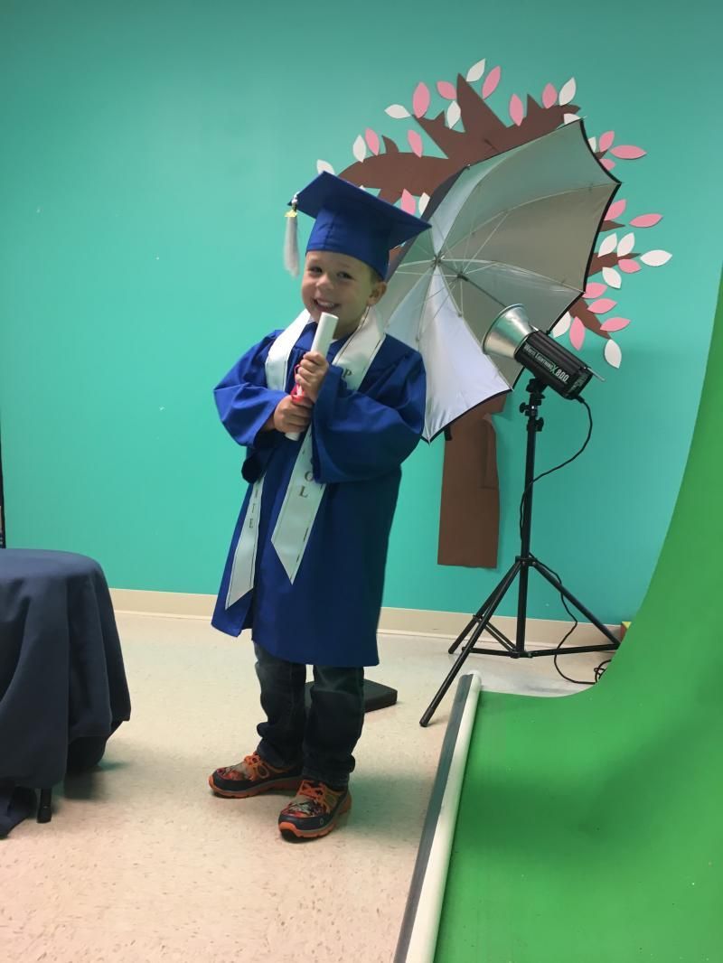 A young boy in a graduation cap and gown holding an umbrella