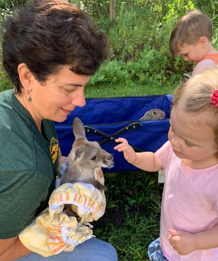 A woman is holding a baby kangaroo while a little girl looks on.