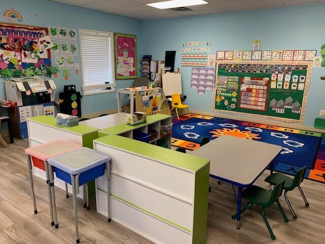 A classroom with tables and chairs and a blue rug.