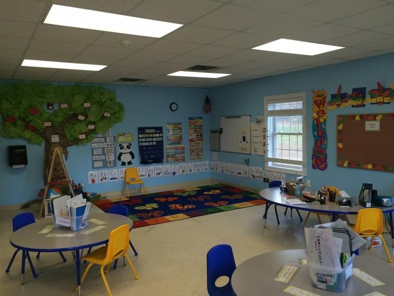 A classroom with tables and chairs and a tree on the wall