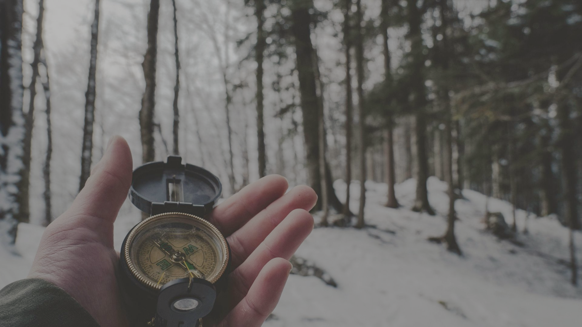 Hand holding an open compass in a snowy forest.