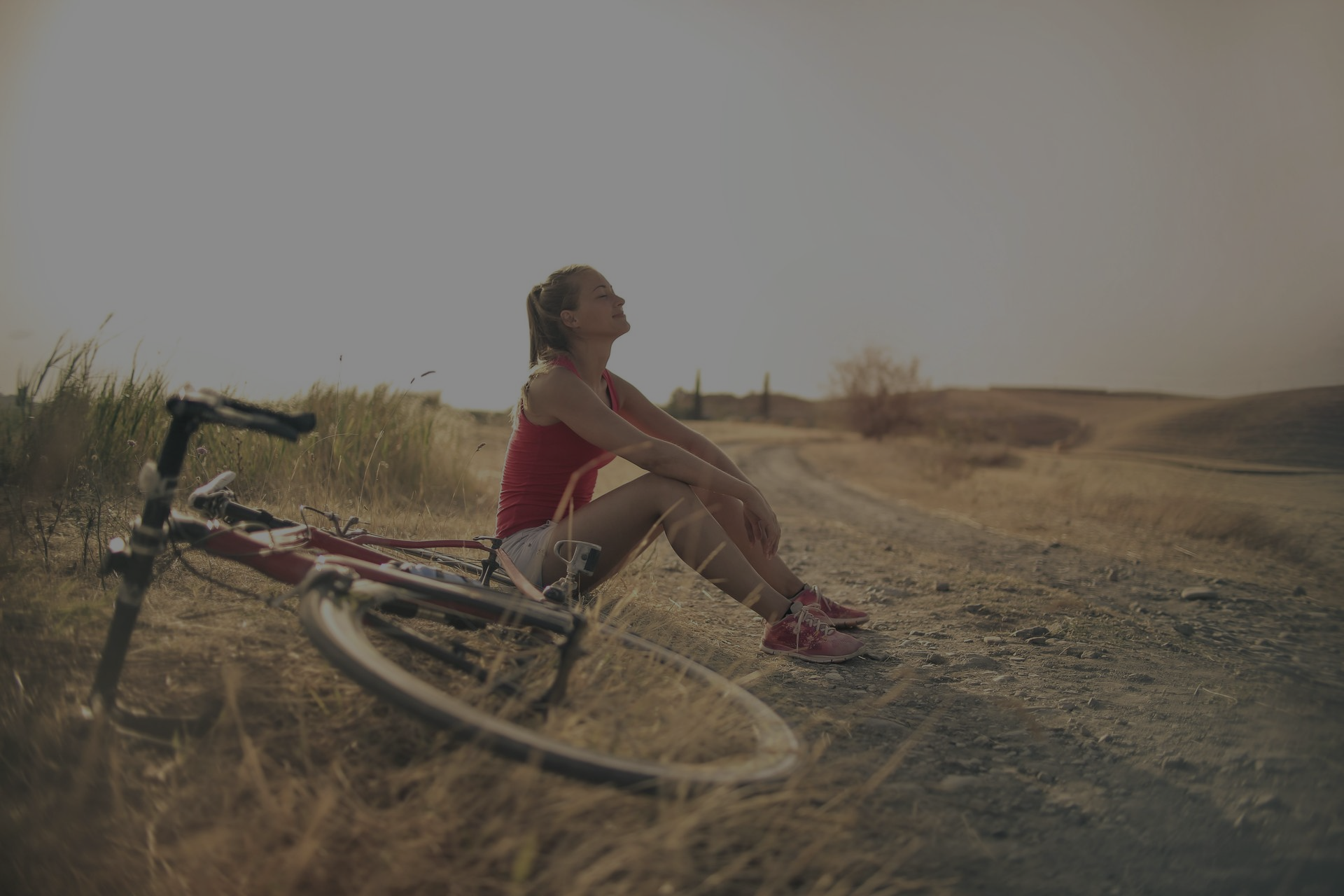 Woman resting by her bicycle on a dirt road, looking up at the sky.