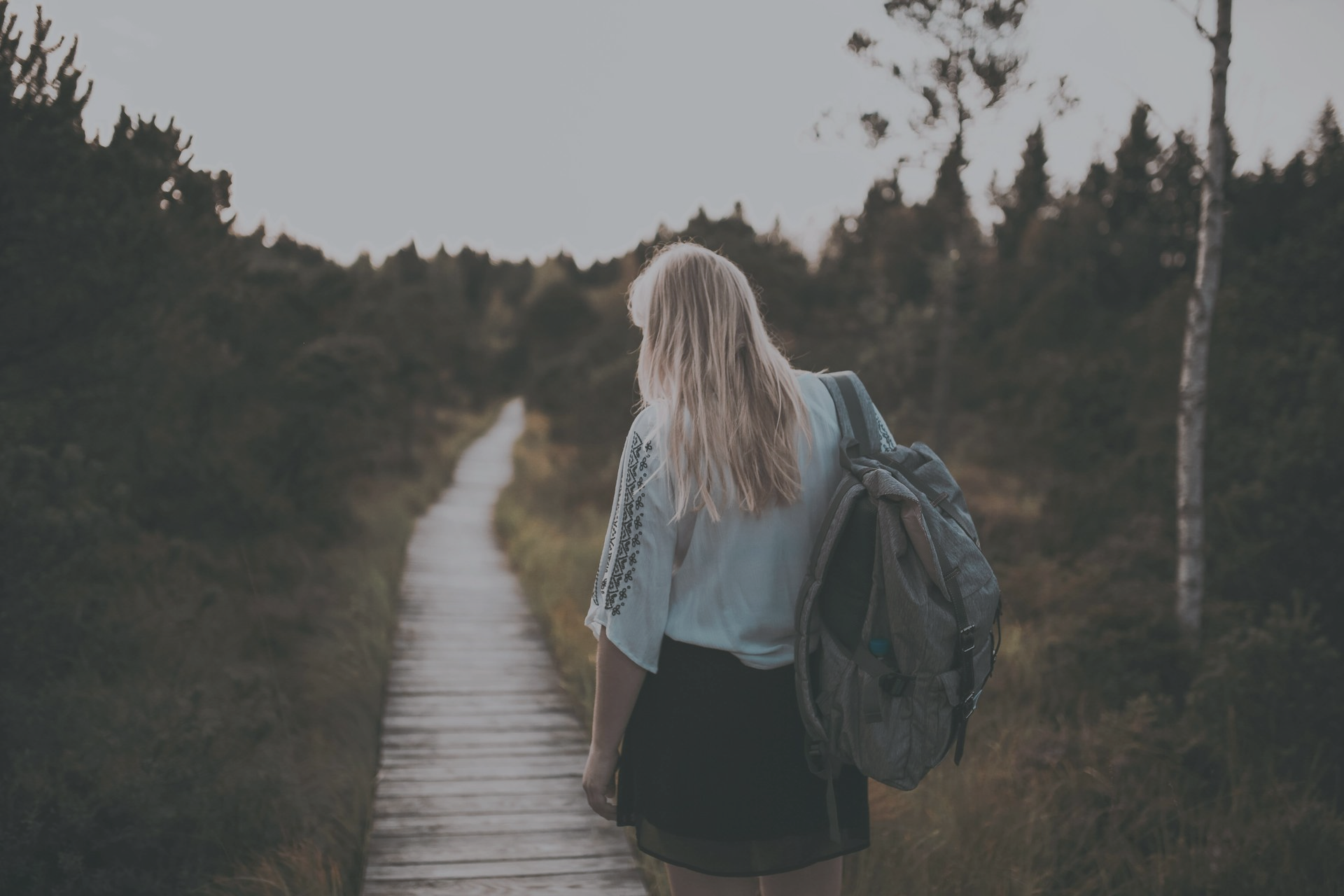 Woman with backpack walks along a wooden path through a forest.