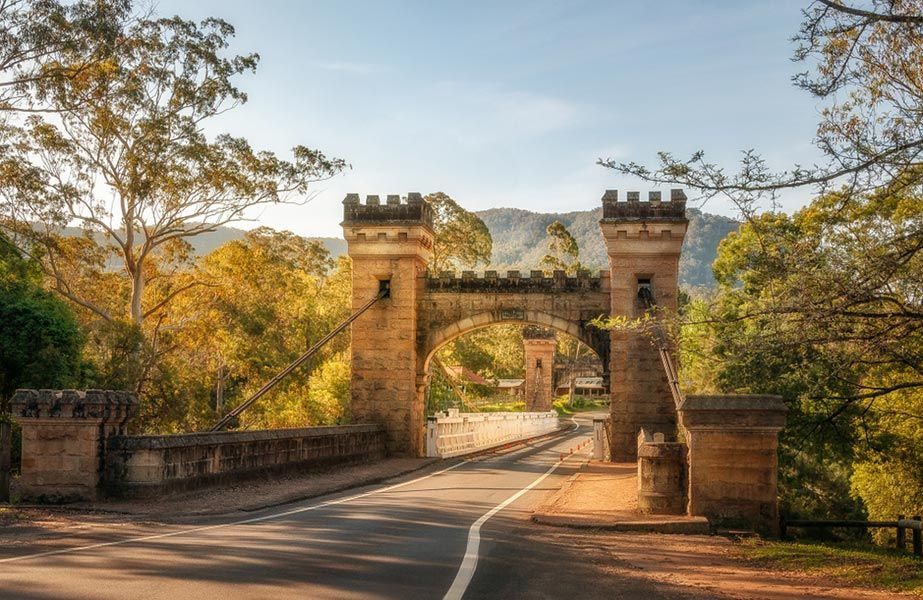 A Bridge Over a Road with Trees in The Background and Mountains in The Background — Burnett Trees in Kangaroo Valley, NSW