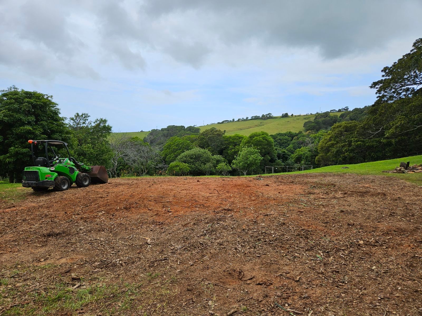 A Yellow Excavator Is Sitting in The Middle of A Dirt Field — Burnett Trees in Kiama, NSW