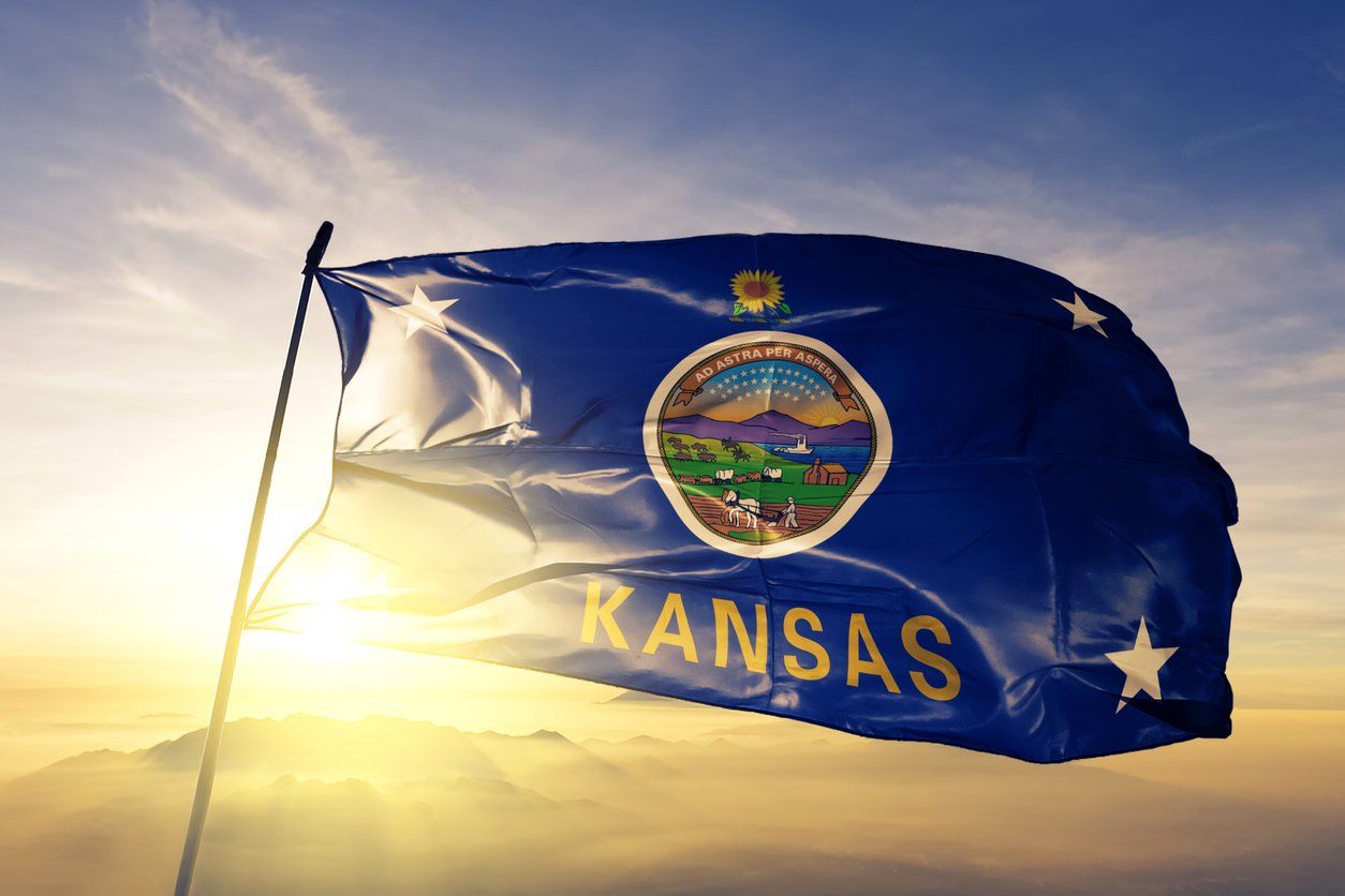 A Kansas flag attached to a flagpole with the sunset in the background.