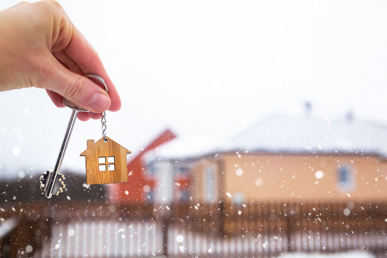 Close-up shot of a hand holding a new key for a house with snow in the background.