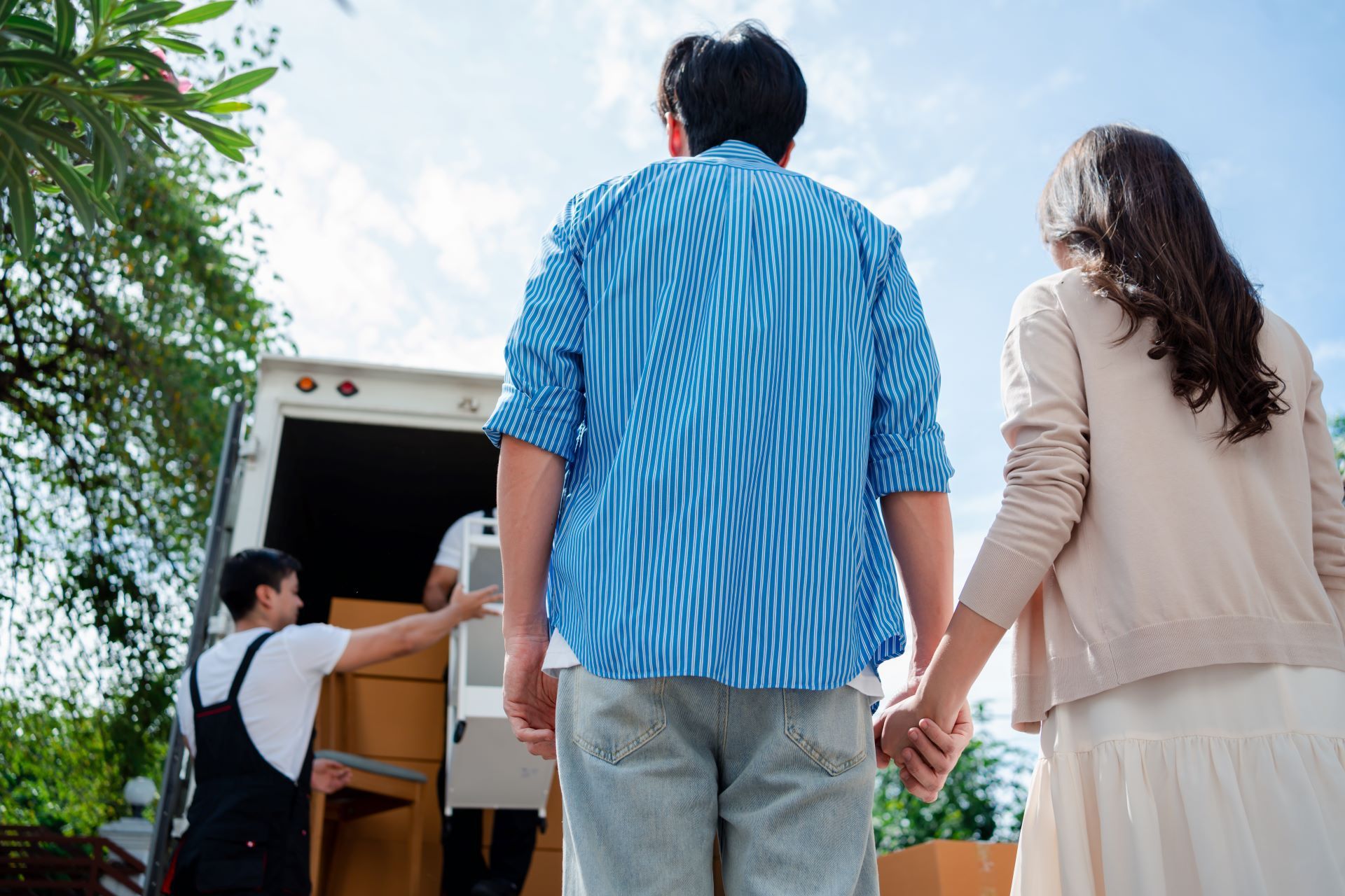 A man and a woman are holding hands while walking towards a moving truck.