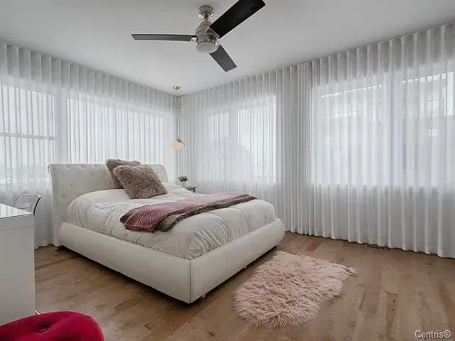 A bedroom with a bed , ceiling fan , and white curtains.