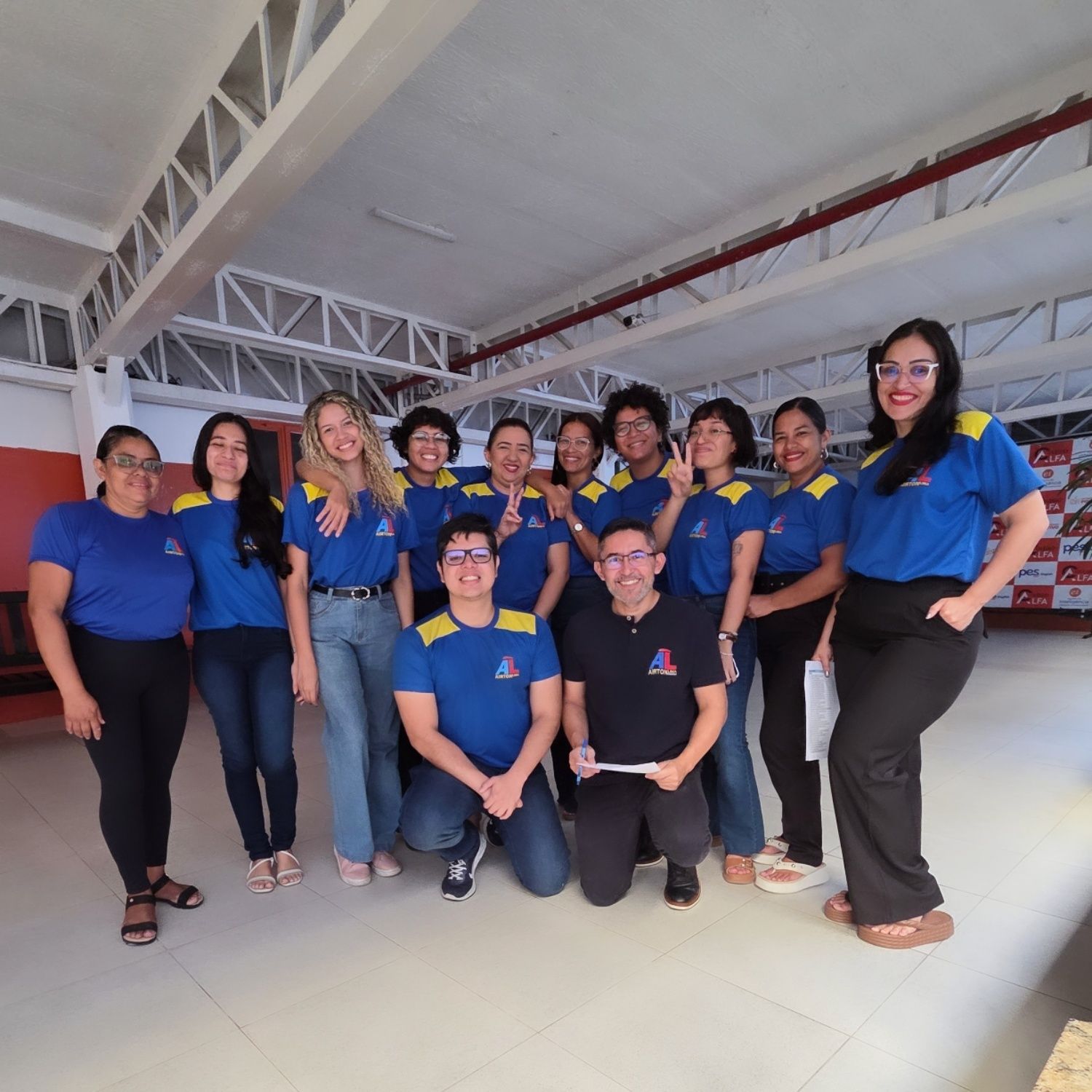 Grupo de pessoas de camisas azuis posam em ambientes fechados, sorrindo.