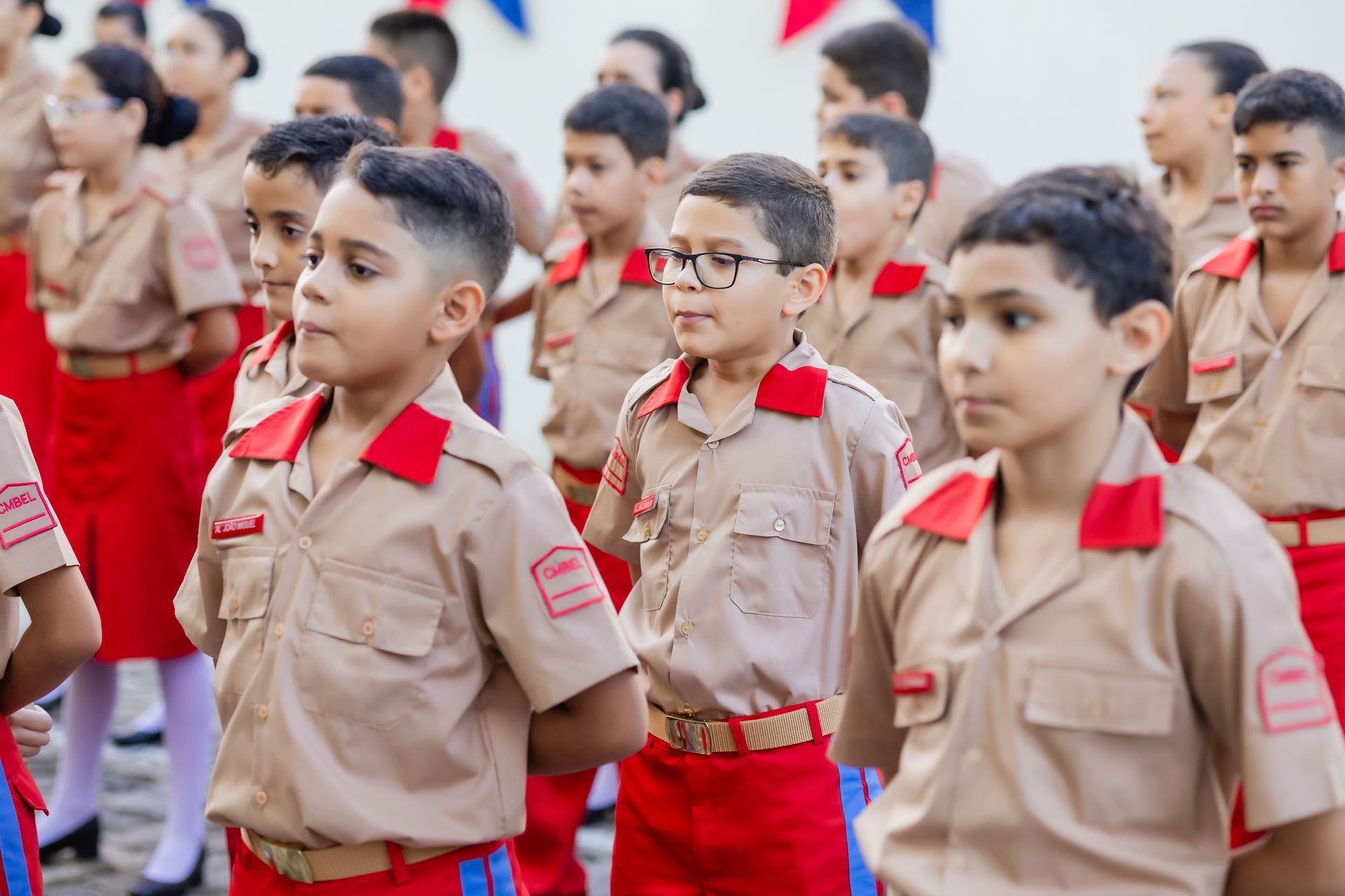 Crianças uniformizadas em formação, algumas com expressões sérias, provavelmente em uma escola ou cerimônia.