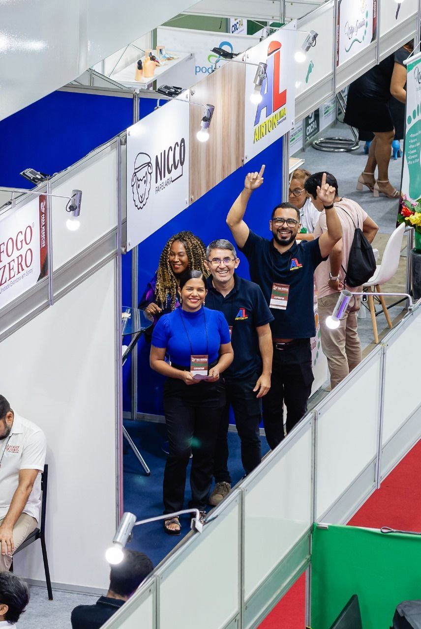 Grupo de pessoas em um estande de feira comercial, sorrindo e comemorando.