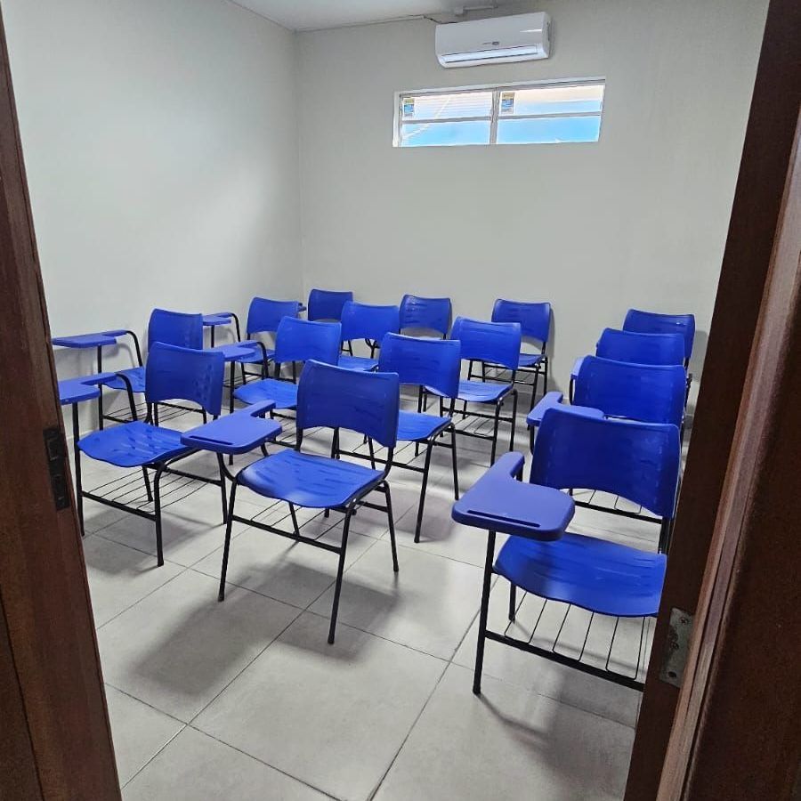 Sala de aula vazia com cadeiras azuis e uma janela.