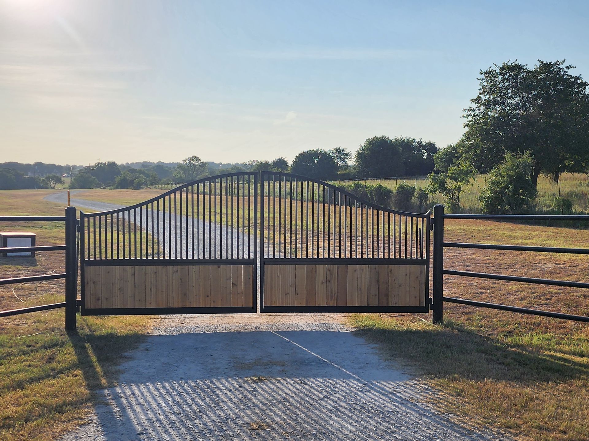 A wooden gate is open to a dirt road