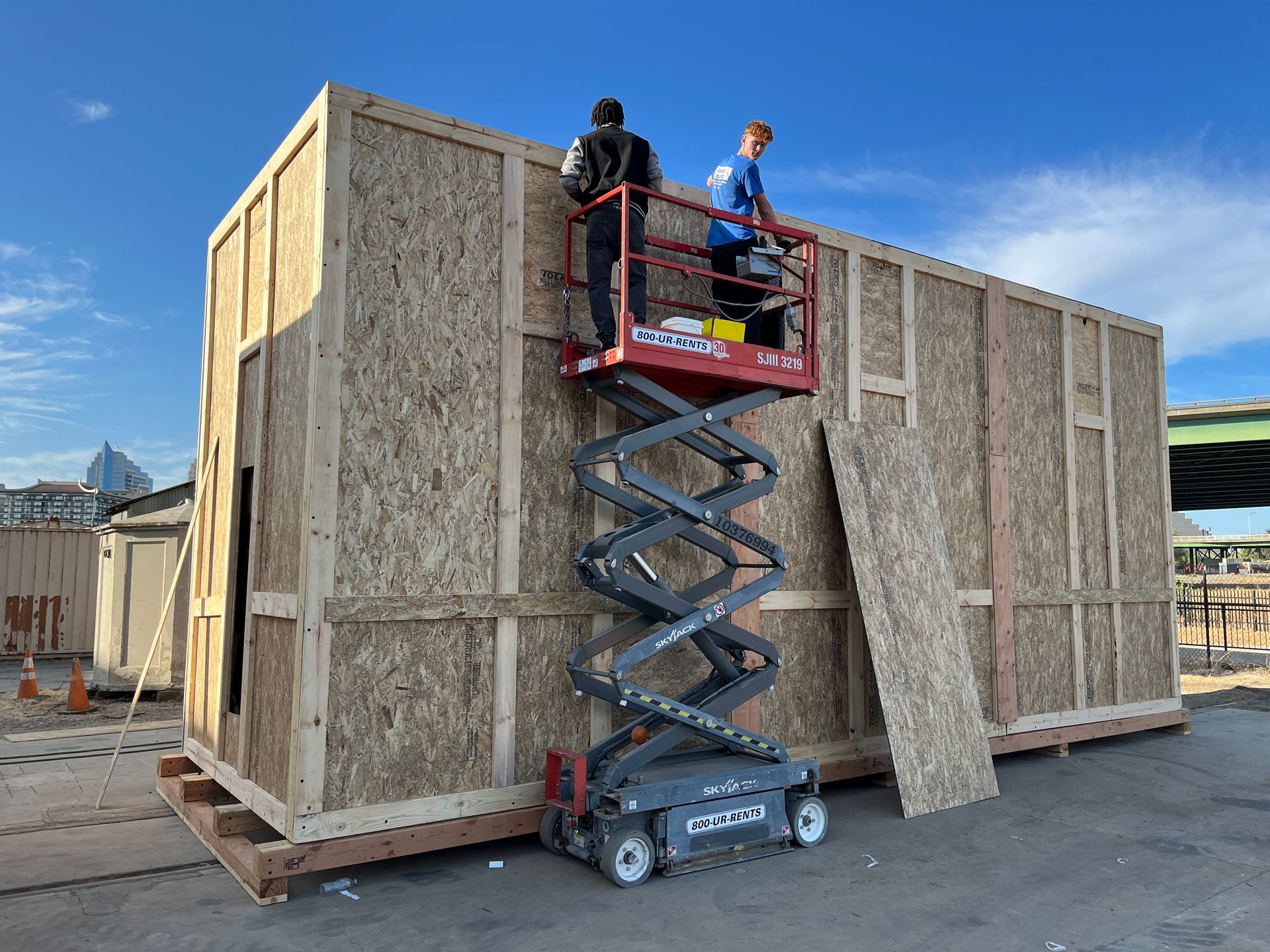 Large wooden crate on a pallet in a warehouse. Gray tarp covers the top of the crate.