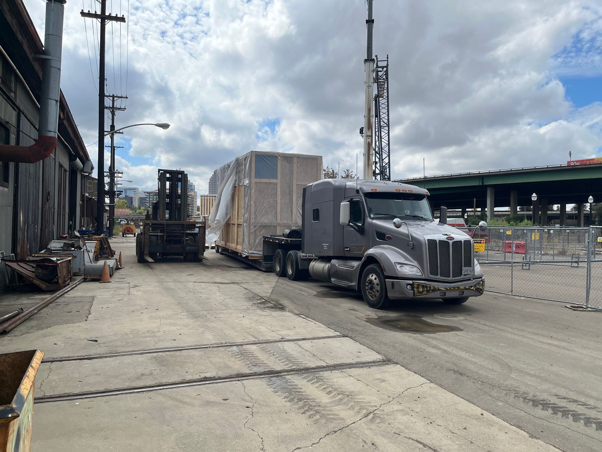 A forklift loading a blue shipping container onto a train car, surrounded by stacked containers.