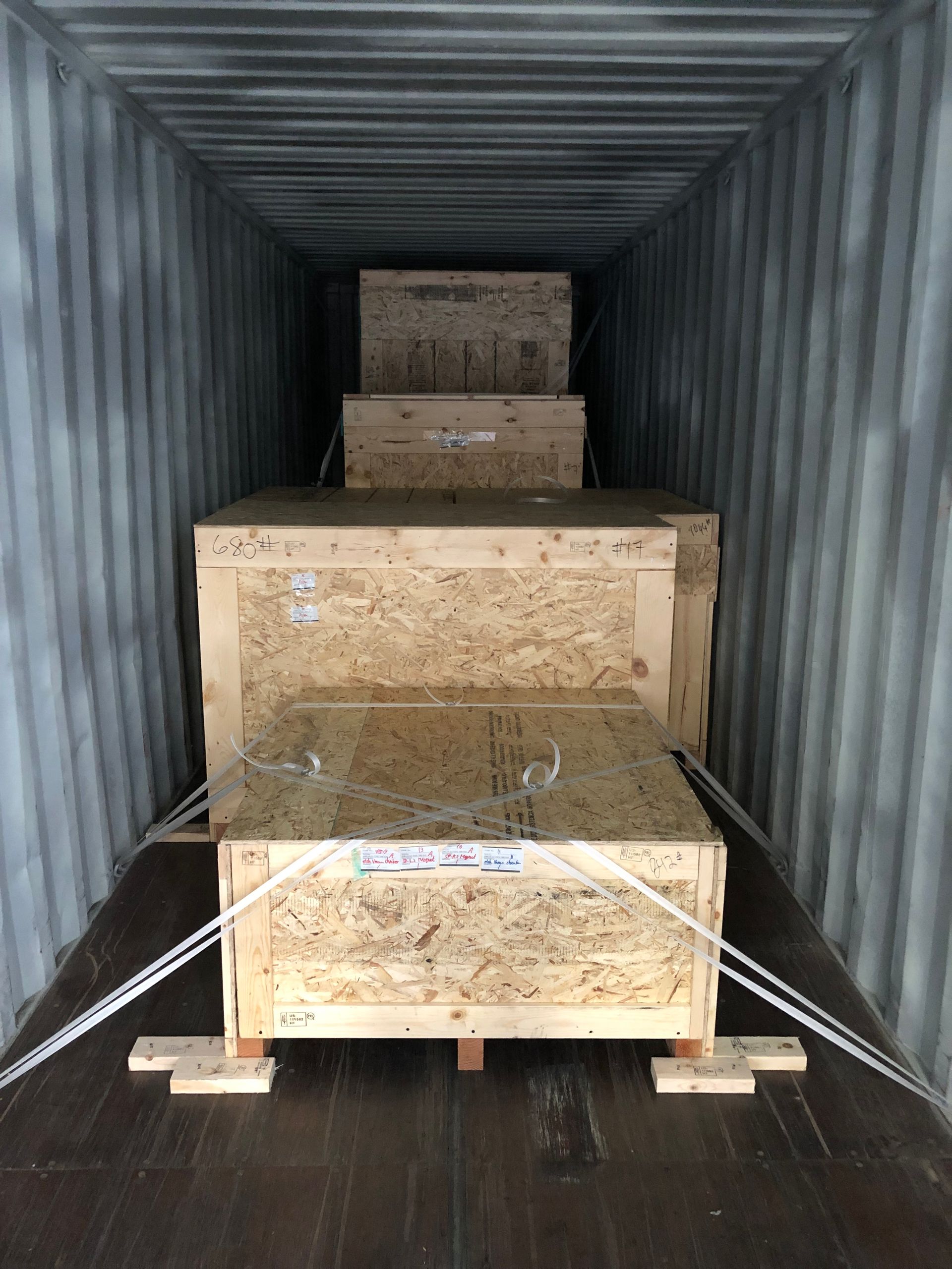 Wooden crate containing cardboard boxes, with additional boxes and buckets on a pallet in the background.