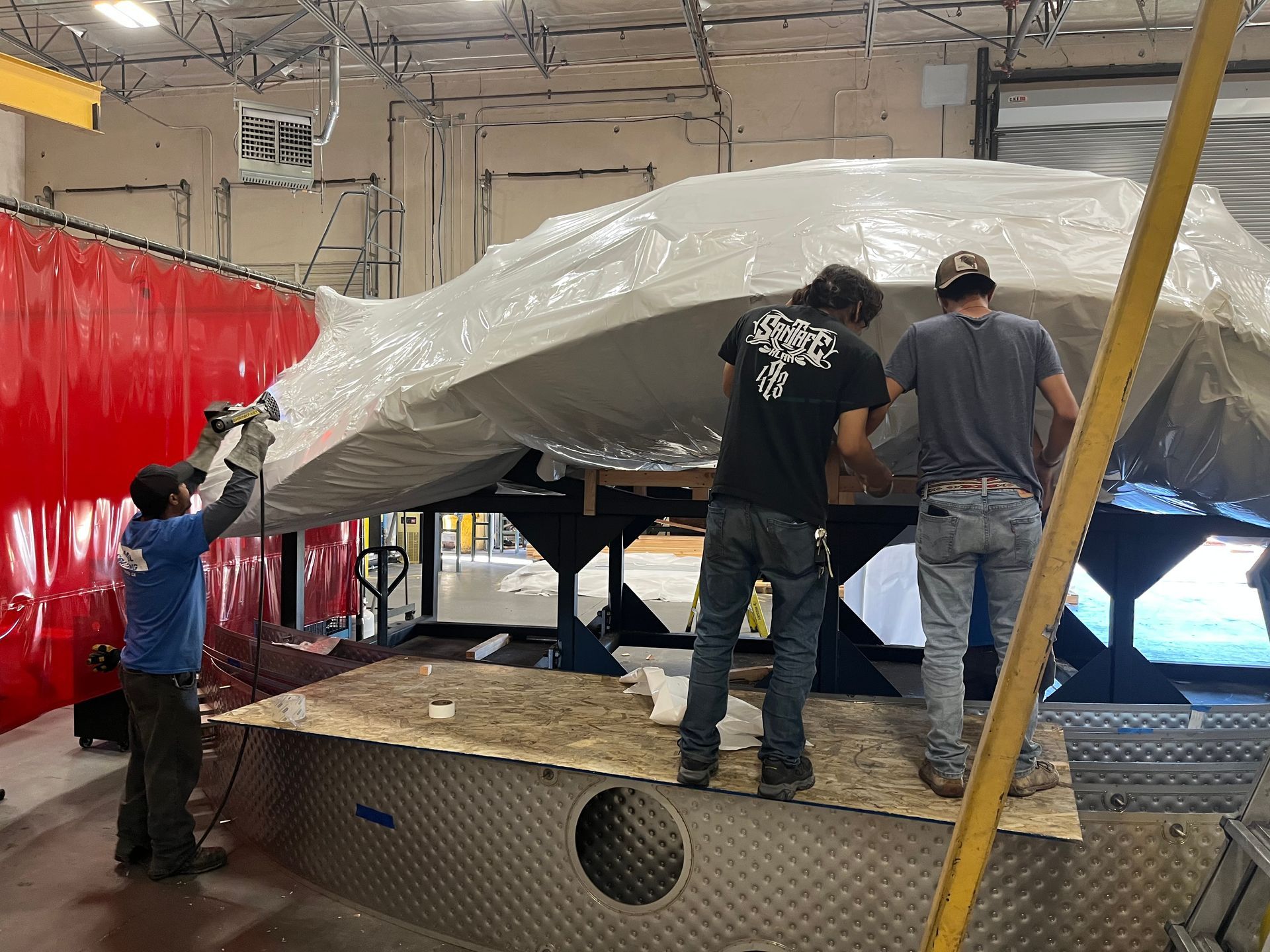 Warehouse worker in yellow vest wrapping boxes on a pallet with clear plastic.