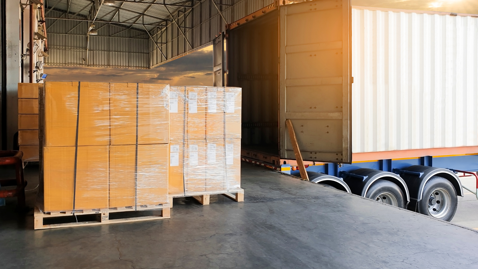 Wooden crate containing cardboard boxes, with additional boxes and buckets on a pallet in the background.
