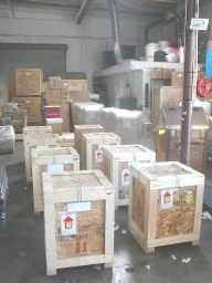 Wooden crates stacked in a warehouse. Various packages, boxes, and machinery are also present.